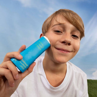 Child holding a blue sunscreen bottle, Attitude Sunly EWG Verified mineral sunscreen face stick SPF 30 for kids,  against a clear sky