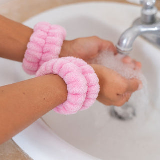 Child washing hands at a bathroom sink while wearing soft pink plush wristbands to keep water from running down the arms