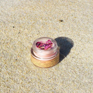 Small container of unicorn lip balm by Plant Makeup - pink lip gloss and dried flowers on sand