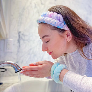 Girl washing hands and face with colorful tie-dye plush headband and wristbands in a bathroom setting