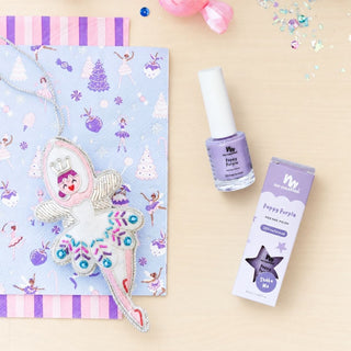 Sugarplum Fairy Ornament and Poppy Purple nail polish with its box, arranged on pastel holiday paper and light wood.
